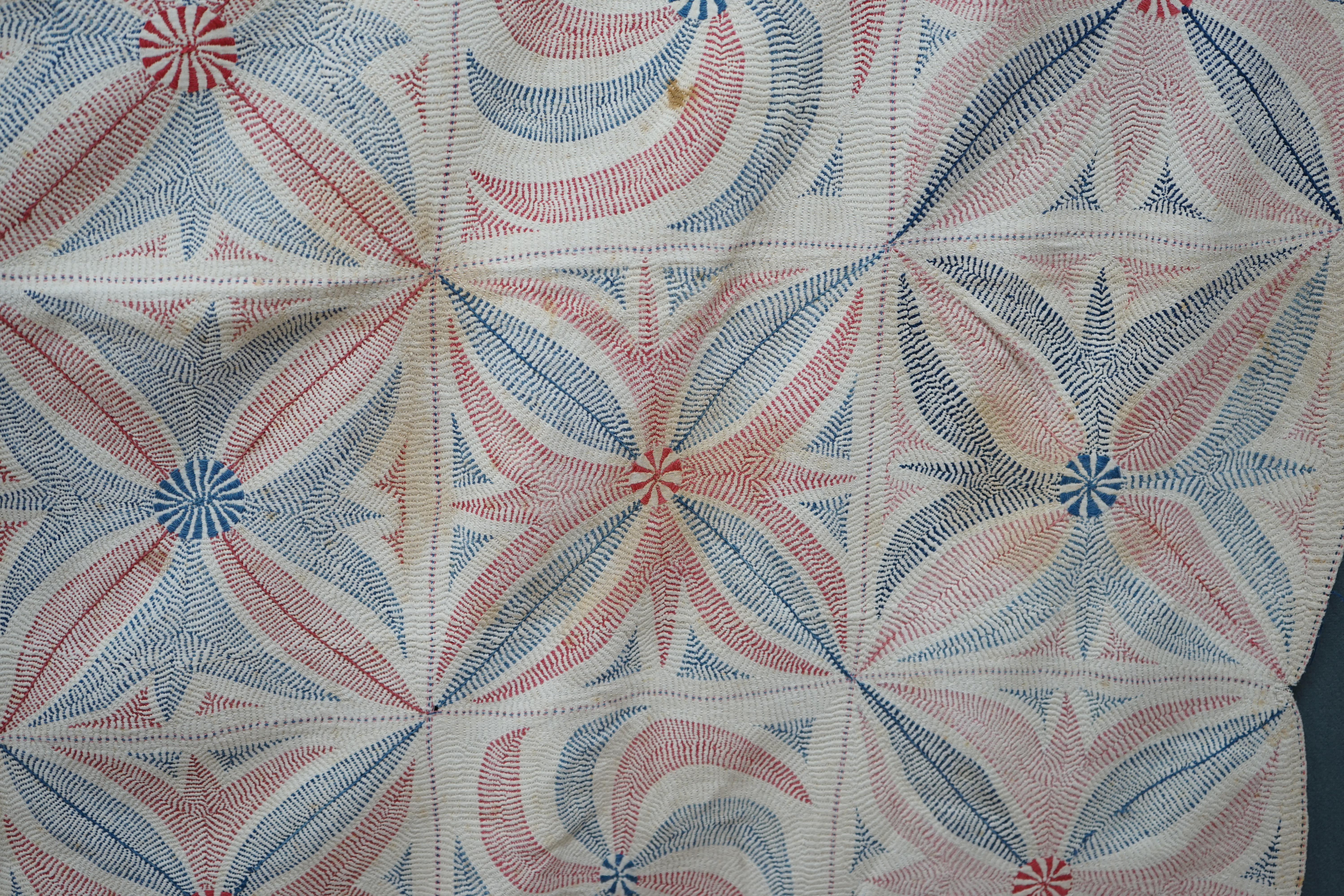 An early 20th century West Bengal Kantha embroidered quilt, embroidered on cream cloth (possibly made from layers of old saris) embroidered in blue and red threads, designed in squares of large abstracted floral motifs u